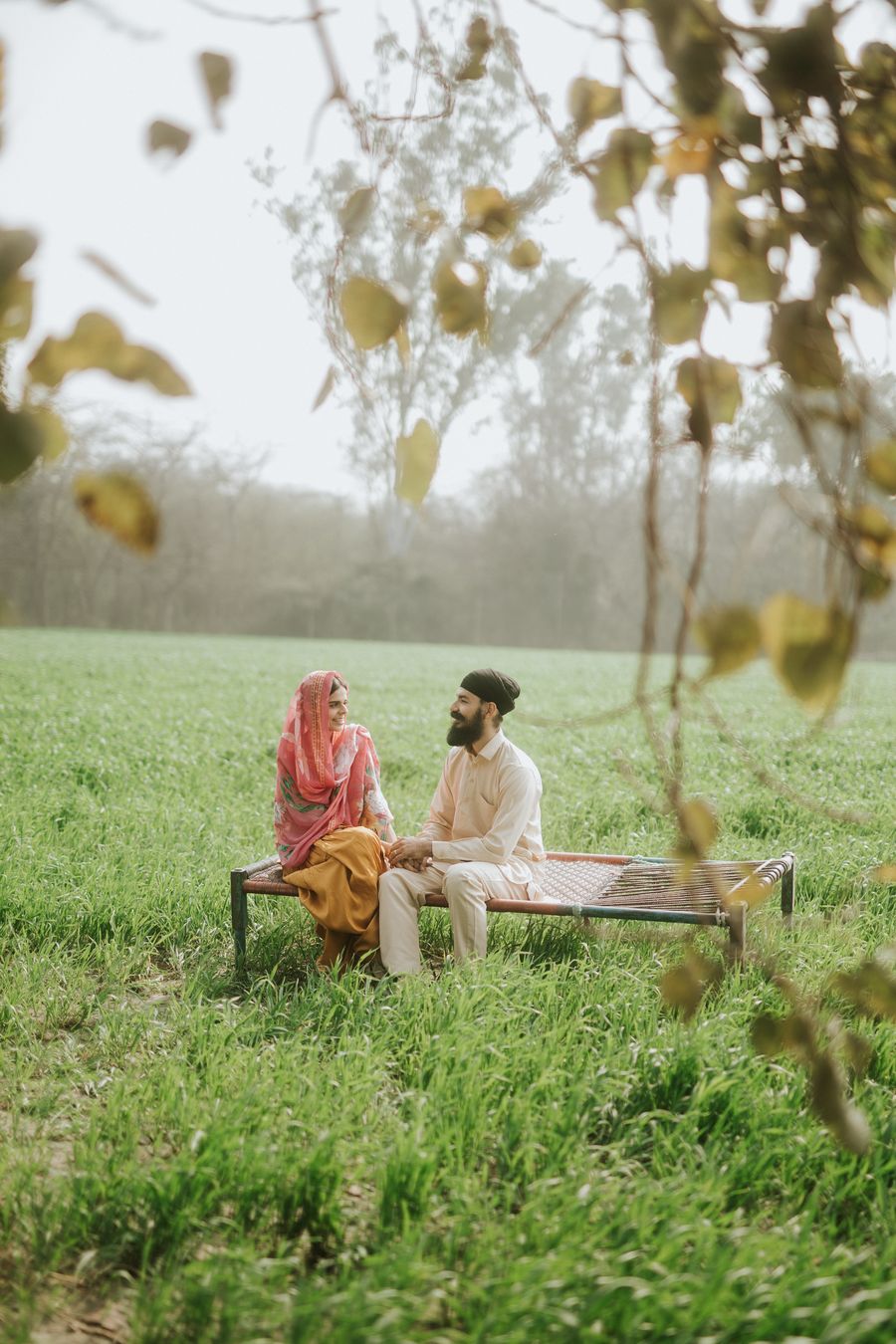 Naaz and Himmat on the charpai in the fields, seen through the leaves